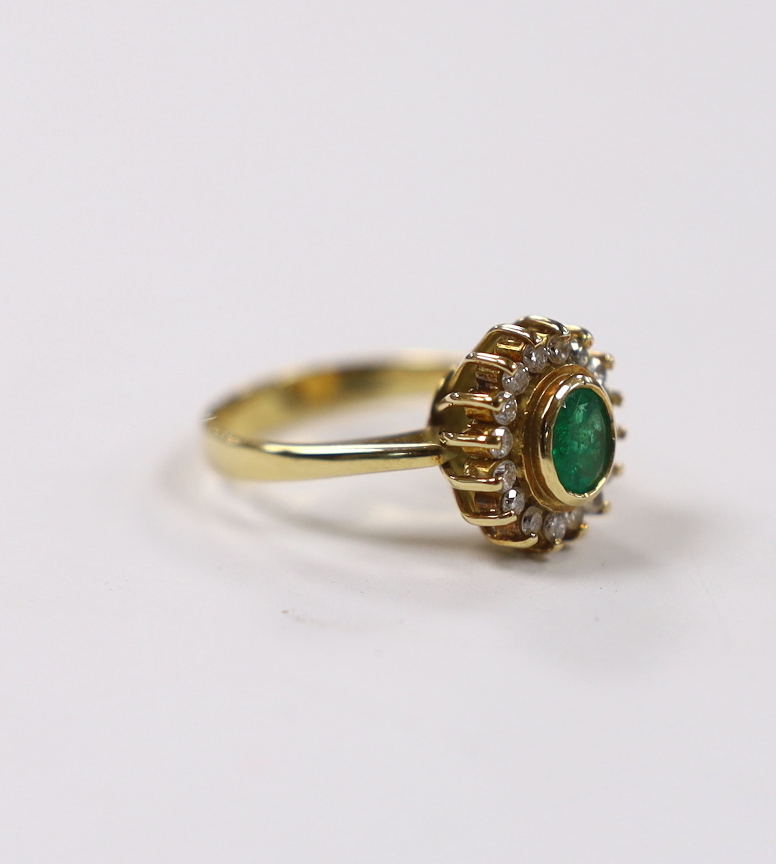 An 18k, emerald and diamond set oval cluster ring, size L, gross weight 5 grams.